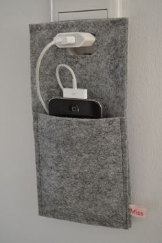 a cell phone is hooked up to a wall charger in a felt pocket that holds an iphone