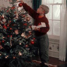 a little boy standing next to a christmas tree