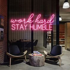 two chairs sitting in front of a neon sign that reads work hard stay humble