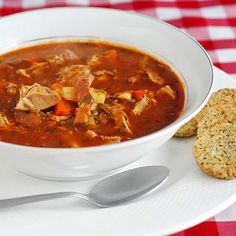 a white bowl filled with soup next to some crackers and a red checkered table cloth