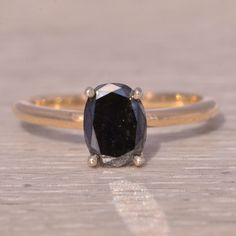 a black diamond ring sitting on top of a wooden table next to a white and gold band