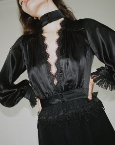 Our Rita Blouse in black features a plunging V neckline trimmed with delicate Venise lace, a true waistline cinch and soft billowing sleeves all trimmed with Alençon lace and embroidered ruffled tulle lace. 100% Silk Charmeuse lined with Silk Habutai Three satin covered pearl buttons for each closure Dry clean only Each piece is made to order and handcrafted in our atelier. Slight variations may occur as each piece is unique. Black Lace Trim V-neck Top, Wedding V-neck Blouse With Ruffles, Elegant V-neck Blouse With Lace Patchwork, Elegant Black Tops With Contrast Lace, Elegant Lace Top For Date Night, Party V-neck Blouse With Lace Patchwork, Feminine V-neck Lace Top For Party, V-neck Lace Trim Top For Night Out, V-neck Blouse With Lace Patchwork For Party