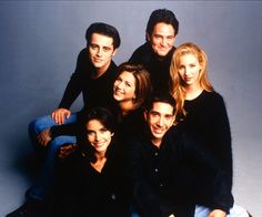 a group of people sitting next to each other in front of a gray background with one person smiling at the camera