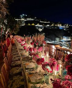 a long table is set up with candles and flowers for an elegant dinner overlooking the city at night