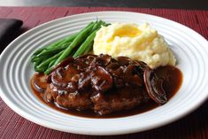 a plate with mashed potatoes, green beans and meat in gravy on it