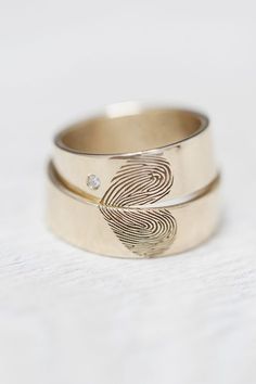 two gold wedding bands with fingerprints on the side and a diamond in the middle