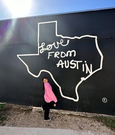 a woman standing in front of a black wall with the words love from texas written on it