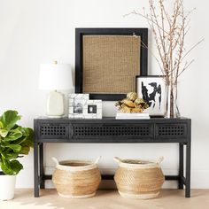 a black table with two baskets on it next to a plant and a framed photograph