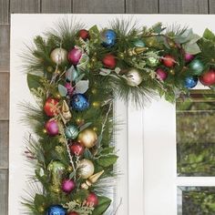 a christmas wreath is hanging on the front door with ornaments and greenery around it