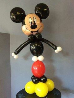 a mickey mouse balloon sculpture on top of a black table with balloons in the air