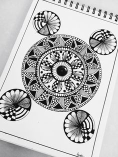 a spiral notebook with black and white designs on it, sitting next to a pen