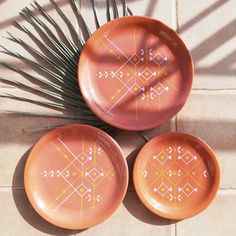 three orange plates sitting on top of a tile floor next to a palm leaf and plant