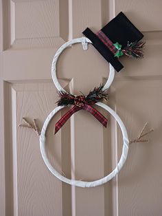 a wreath on the door with a hat hanging from it's top and ribbon