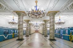 an empty train station with blue and white trains in the background, chandelier hanging from the ceiling