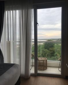 a bedroom with an open door leading to a balcony overlooking the ocean and trees in the distance