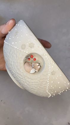 a person holding a white vase with red dots on it's side and a silver object in the middle