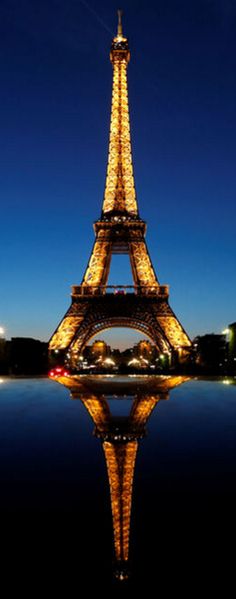 the eiffel tower lit up at night with its lights reflecting in the water