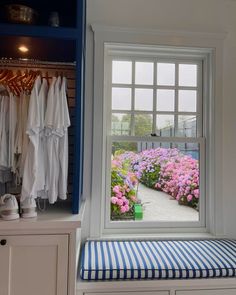 an open window with flowers and clothes hanging on the rack next to it, in front of a white wall