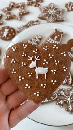 a hand holding a heart shaped gingerbread with white frosting and reindeer decorations on it