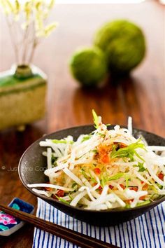 a black bowl filled with coleslaw on top of a table next to chopsticks