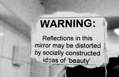 a black and white photo of a sign warning people to reflect in this mirror may be distorted by socially constructed ideas of beauty