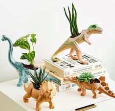 three dinosaur figurines sitting on top of books with plants growing out of them