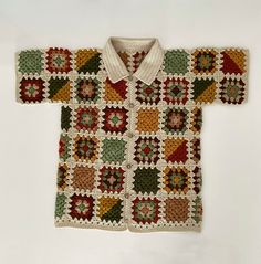 a crocheted shirt is sitting on a white surface and it's made out of multicolored squares