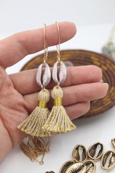 a pair of earrings with tassels in the shape of seashells is being held by a woman's hand