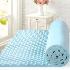 a rolled up blue mat sitting on top of a bed next to a vase with flowers