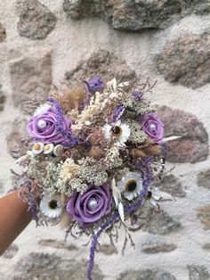 a bridal bouquet with purple and white flowers is held up against a stone wall