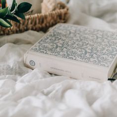 a white book sitting on top of a bed next to a basket with flowers in it