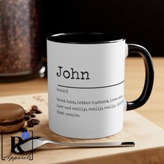 a black and white coffee mug sitting on top of a wooden table next to a cookie