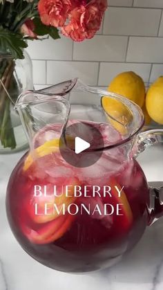 a pitcher filled with liquid sitting on top of a counter next to lemons and flowers