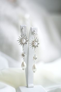 a pair of white pearl and crystal earrings on a white surface with blurry background