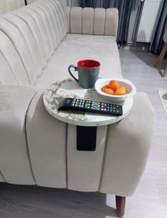 a table with a remote control, bowl of oranges and a coffee cup on it