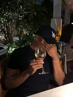 a man sitting at a table with a wine glass in front of him and covering his face