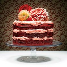 a red cake sitting on top of a glass plate covered in frosting and flowers