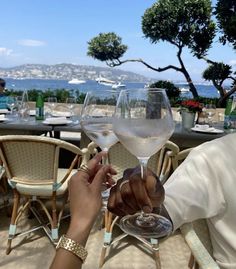 two people toasting with white wine at an outdoor table overlooking the ocean and mountains