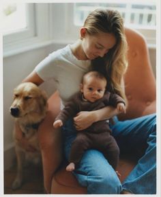 a woman holding a baby sitting next to a dog