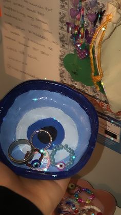 a hand holding a blue bowl with rings in it and beads on the rim around it