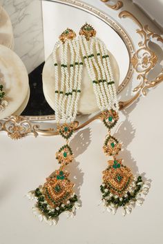 The "Sanjana - Long Saharay Earrings and Maang Tikka set" is an embodiment of imperial classics and a celebration of the richness of Navratan stones. This exquisite set is curated to evoke the essence of grandeur and festivity. The set includes a dazzling maang tikka and a pair of brilliant earrings, each adorned with breathtaking stonework and pearl moti, reflecting sheer class. The earrings feature saharay and a Navratan motif at the tip, creating an alluring visual spectacle. With an approxim Green Meenakari Bridal Earrings For Reception, Green Bollywood Chandelier Earrings With Meenakari, Maang Tikka Earring Set, Elegant Green Meenakari Earrings, Green Meenakari Dangle Earrings, Maang Tikka Set, Ear Chain, Chandbali Earrings, Accessories Ear