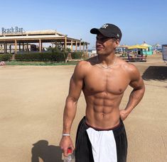 a shirtless man holding a water bottle in his hand and standing on the beach