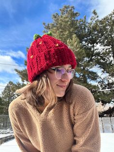 a woman sitting in the snow wearing a red knitted hat