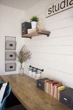 a wooden table topped with lots of books next to a wall mounted shelf filled with boxes