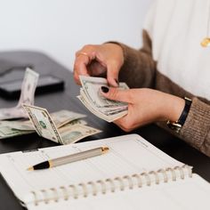 a woman is counting money at her desk with a pen and notebook on the table