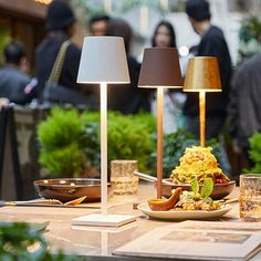 a table with two lamps and plates of food on it in front of some people