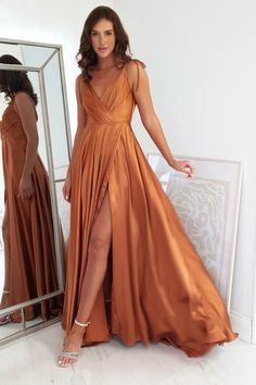 a woman standing in front of a mirror wearing an orange dress with thigh high slit