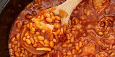 a wooden spoon in a slow cooker filled with beans and meats, ready to be cooked