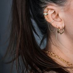 a close up of a person wearing gold ear rings and chain necklaces, with their hair pulled back to the side