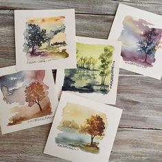 five watercolor cards with trees on them sitting on top of a wooden table next to each other